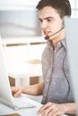 Casual dressed young man using headset and computer while talking with customers online in sunny office. Call center Royalty Free Stock Photo