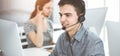 Casual dressed young man using headset and computer while talking with customers online in sunny office. Call center Royalty Free Stock Photo