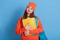 Casual girl student with bag backpack and paper folder isolated over blue background, smiling female wearing orange sweater and Royalty Free Stock Photo