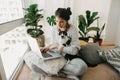 Casual girl working on laptop with her cat, sitting together in modern room with pillows and plants. Home office. Young woman Royalty Free Stock Photo