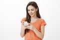 Casual good-looking urban girl in orange t-shirt, messaging with friend via smartphone, listening music in earphones Royalty Free Stock Photo