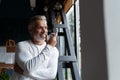 Casual Grey-haired Mature businessman talking on a mobile phone standing by the window. Royalty Free Stock Photo