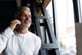 Casual Grey-haired Mature businessman talking on a mobile phone standing by the window. Royalty Free Stock Photo