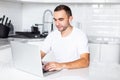 Young man calling on cell phone via airpods while working on laptop computer at home in the morning Royalty Free Stock Photo