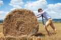 Casual man outdoor looks at you and pushes haystack Royalty Free Stock Photo