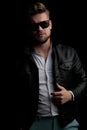 Casual man wearing sunglasses standing and fixing his leather jacket Royalty Free Stock Photo