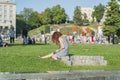 Casual student girl writing in the diary outdoors. Slim girl with curly red hair sitting on the grass in city center in Kiev