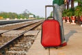 Casual traveler tourist legs stand on railway with a red suitcase