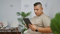 Casual young latin man, plugged into his online world, sitting relaxed in a waiting room chair, intensely interacting with his Royalty Free Stock Photo