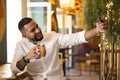 Young latino guy taking a picture with his smart phone while showing smiling cocktail in his hand