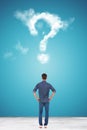 Casual young man looking at a big question mark made of clouds Royalty Free Stock Photo