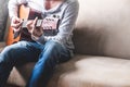 Casual young man playing guitar on sofa at home. Royalty Free Stock Photo