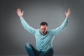 Casual young man sitting on the floor with his legs crossed and cheering with his hands in the air while screaming. Royalty Free Stock Photo