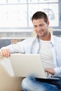 Casual young man using laptop at home smiling Royalty Free Stock Photo