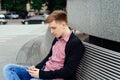 Casual young man using smart phone sitting on bench in city. Royalty Free Stock Photo