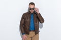 Casual young man wearing brown leather jacket looking over sunglasses Royalty Free Stock Photo