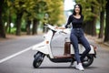 Casual young woman sitting on moto scooter on narrow street in town.