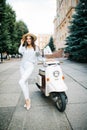 Young woman sitting on moto scooter on narrow street in old town.