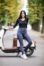 Casual young woman sitting on moto scooter on narrow street in town.