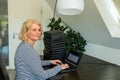 A casually dressed caucasian middle aged woman is installing a laptop computer with a stack of several more computers