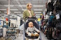 Casualy dressed mother choosing sporty shoes and clothes products in sports department of supermarket store with her