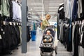 Casualy dressed mother choosing sporty shoes and clothes products in sports department of supermarket store with her