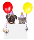 Cat and dog in birthday hats holding balloons peeking from behind empty board Royalty Free Stock Photo