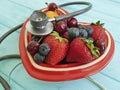 Cat homeless eats on the delicious strawberry, antioxid sweet blueberry, cherry, apricot plate heart on blue wooden, stethoscope