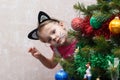 Cat painted little girl peeking out from behind Christmas tree