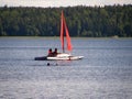 Catamaran with a red sail on the lake against the backdrop of the forest. Royalty Free Stock Photo