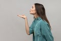 Side view of lovely romantic young woman looking ahead air kissing over palms hands, sending love.