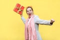 Catch your gift! Young adult crazy woman swung and wants to throw off your gift box, isolated on yellow background.