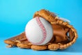 Catcher\'s mitt and baseball ball on light blue background, closeup. Sports game