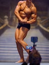 Catching it all on camera. Rearview of a cameraman filming a bodybuilder flexing his muscles during a competition.