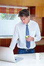 Catching up with emails first thing. A young man browsing on his laptop in the kitchen while enjoying a snack.