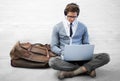 Catching up on his emails while he waits for his ride. A handsome young nerd sitting on the ground while typing on his