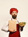 Catering and eating out concept. Cook with serious face in burgundy uniform holds baked dish