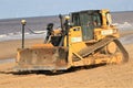 Caterpillar tractor bulldozer on beach with wind turbines