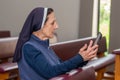 Catholic nun in a chapel pew and looking at a tablet which she is holding.