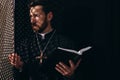 Catholic priest in cassock holding Bible and talking to parishioner in confessional