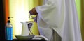 Modern times Churches confronting global pandemic. Priest serving mass with hand sanitizer pump bottle alongside