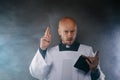 Catholic priest in white surplice and black shirt with cleric collar reading bible