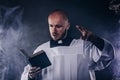 Catholic priest in white surplice and black shirt with cleric collar reading bible