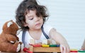 Caucasian adorable cute curly hair little girl wearing white shirt, staying alone, playing toys and doll in living room at home