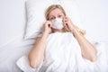 Caucasian adult woman lying in bed with flu, cold and fever, she is sick and wearing face mask