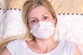 Caucasian adult woman lying in bed with flu, cold and fever, she is sick and wearing face mask