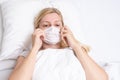 Caucasian adult woman lying in bed with flu, cold and fever, she is sick and wearing face mask