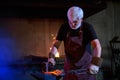 Caucasian aged blacksmith hitting molten metal with hammer