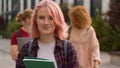 Caucasian alone lonely student girl with pink hair walking smiling at camera holding book walk in city outdoors