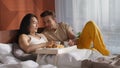 Caucasian and asian men sitting on bed in cozy apartment and enjoying breakfast Royalty Free Stock Photo